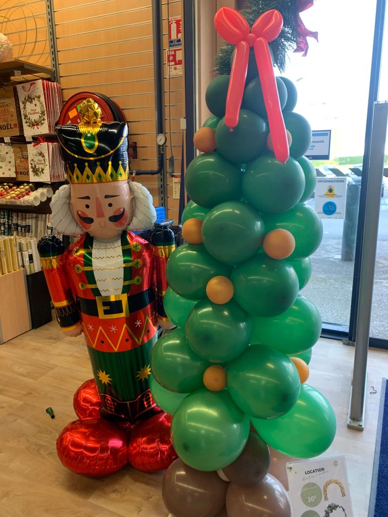 Un sapin avec des ballons de baudruche vert, un pied marron et un joli noeud en guise de cimier.