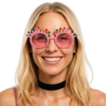 Personne souriante portant des lunettes de soleil fantaisie roses à paillettes avec une monture en forme de couronne ornée de gemmes colorées | jourdefete.com