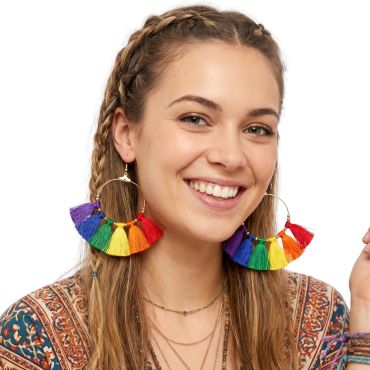 Jeune femme souriante portant des boucles d'oreilles créoles ornées de pompons multicolores arc-en-ciel | jourdefete.com