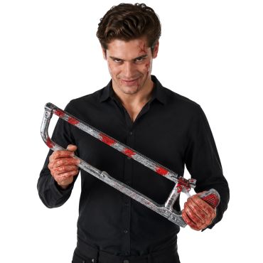 Homme souriant en chemise noire tenant une fausse scie à métaux recouverte de faux sang pour Halloween | jourdefete.com Homme souriant en chemise noire tenant une fausse scie à métaux recouverte de faux sang pour Halloween | jourdefete.com